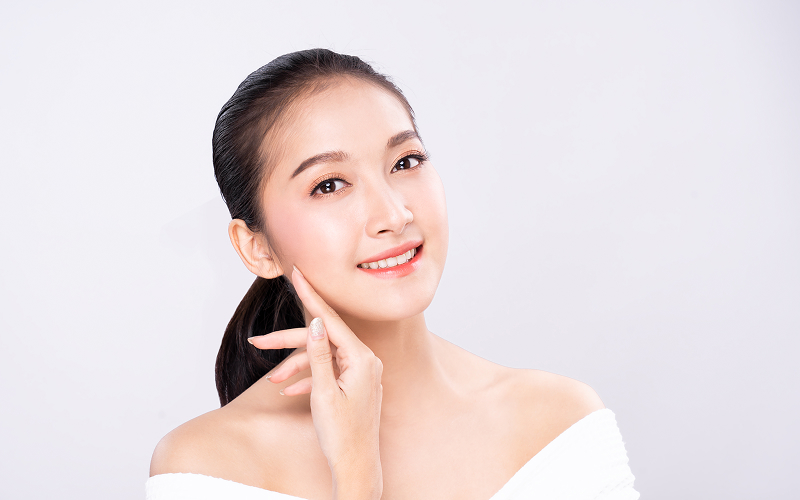 Smiling woman touching glowing face for healthy skin wellness habits.