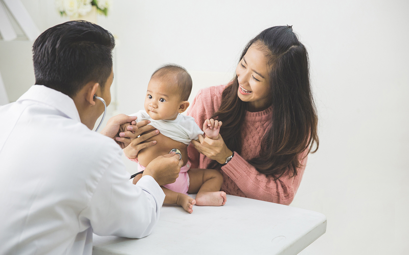 Pediatrician examining baby during mother's postpartum checkup session.