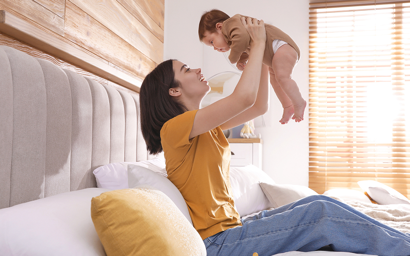 Mother holding newborn baby while resting during postpartum recovery.