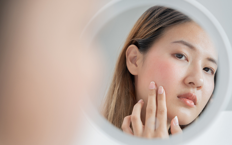 Woman examining dull skin tone in mirror before facial treatment