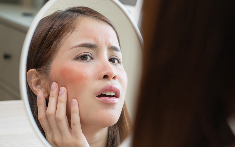 Woman looking in mirror inspecting red irritated skin patc